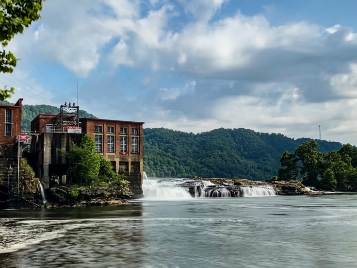 A river-wide waterfall flows over rocks next to an old brick building