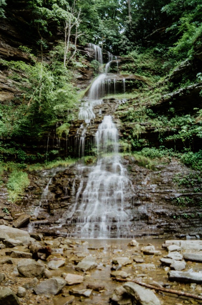 A tall cascading waterfall surrounded by lush green moss and ferns.